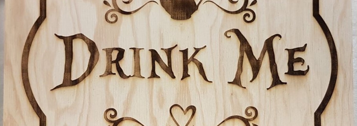 gravure sur bois: texte "Drink Me" et éléments décoratifs